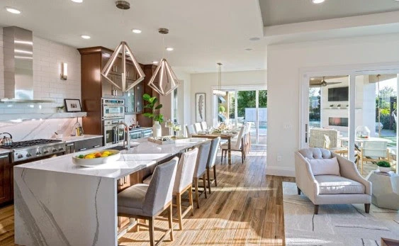 A modern kitchen with a large white island, seating for family, opens to a dining and living area with natural light.
