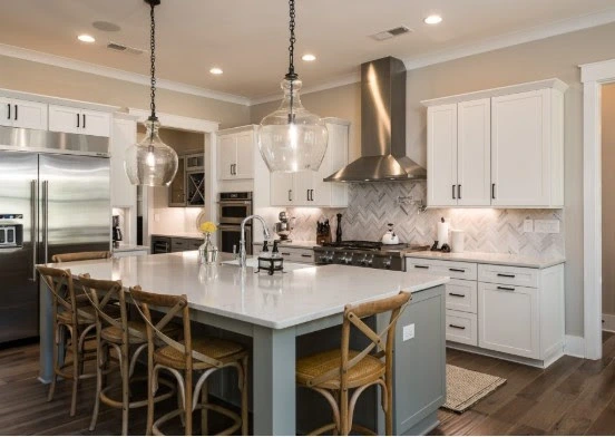 A white kitchen island with stools for family gatherings, surrounded by modern appliances and pendant lights in a cozy kitchen.